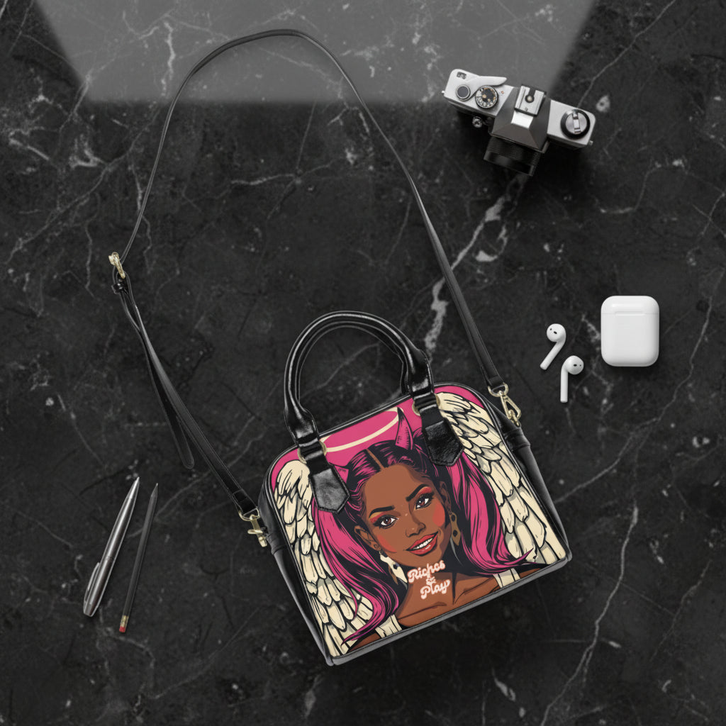 Handbag with artistic design of a devilish angel, accompanied by a camera, earbuds, and pencils on a white background.
